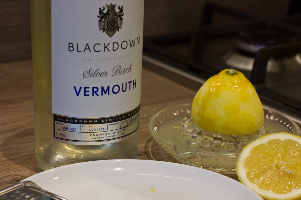 Bottle of Blackdown Vermouth alongside a squeezed lemon half atop a juicer -- prelude to making syllabub